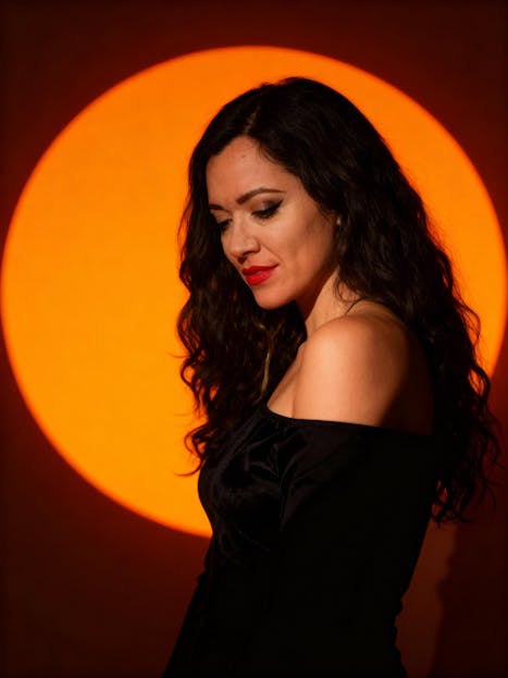 Lupe Gidley Artistic portrait of woman in front of a glowing orange circle, exuding elegance.