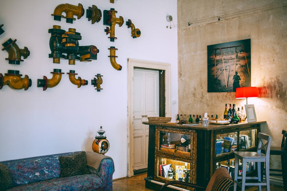 Crackstube Comfortable retro styled room with metal pipes on wall near vintage table with various glass bottles