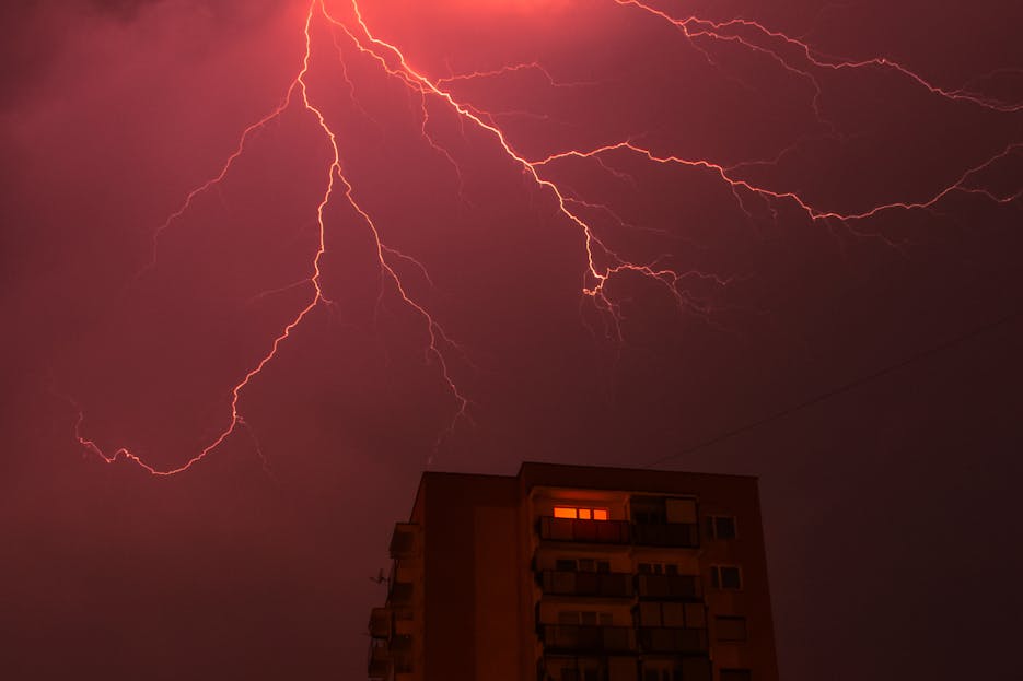 Petir108win.online Intense lightning bolts illuminate the night sky above a city building, showcasing a thrilling weather phenomenon.