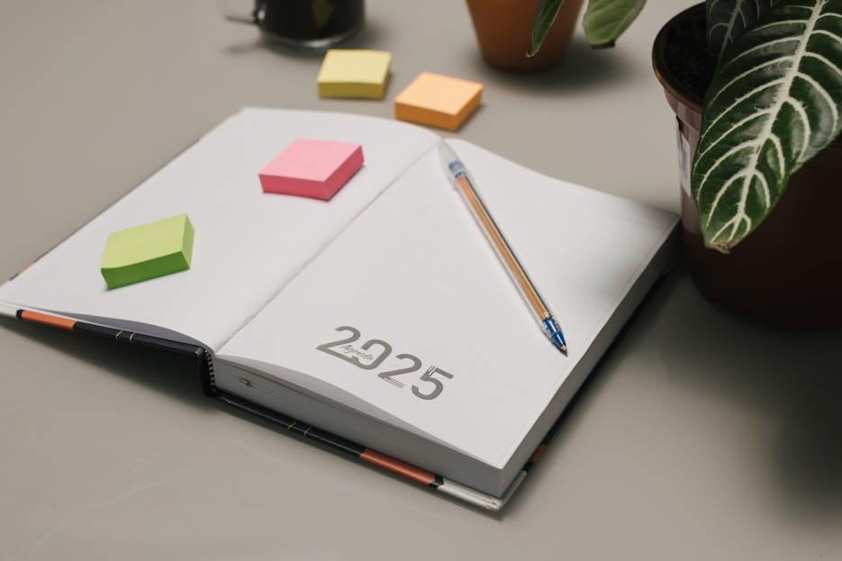 None Company Objectives 2025 Open planner for 2025 with colorful sticky notes and plants on a desk.