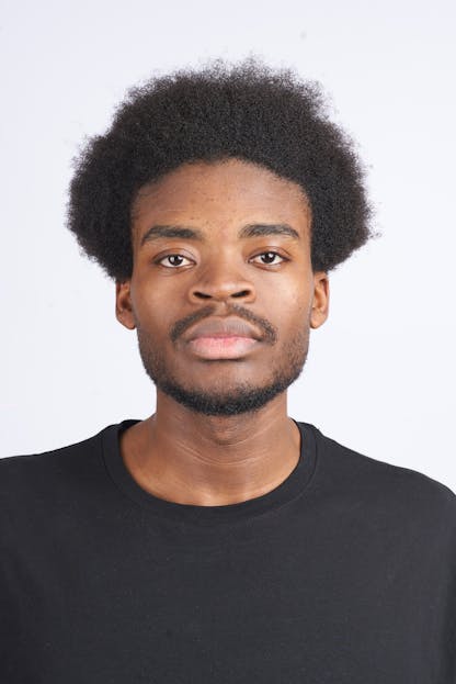 Berniece Julien Professional studio portrait of a man with afro hair wearing a black t-shirt against a white backdrop.
