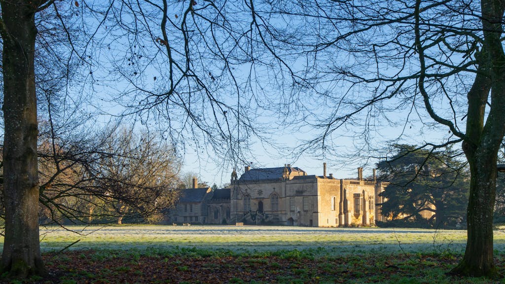 Pabingt Serene view of a historic English manor framed by trees under a clear blue sky.