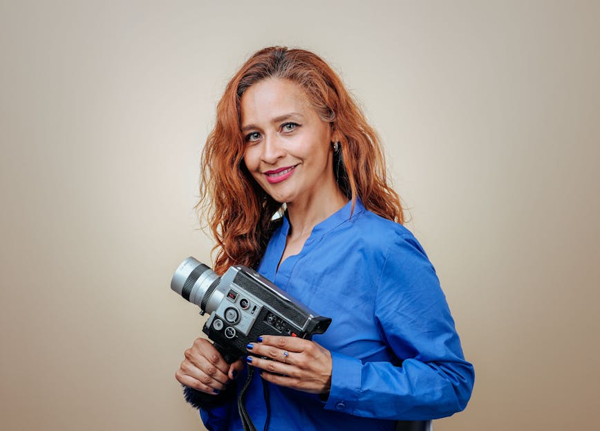 Wendy Etris Smiling woman with red hair holds a vintage camera in a studio setting.