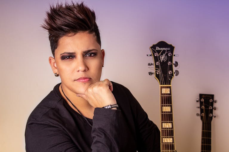 Lupe Gidley Stylish musician posing with electric guitar in a studio setting, exuding confidence and rock attitude.