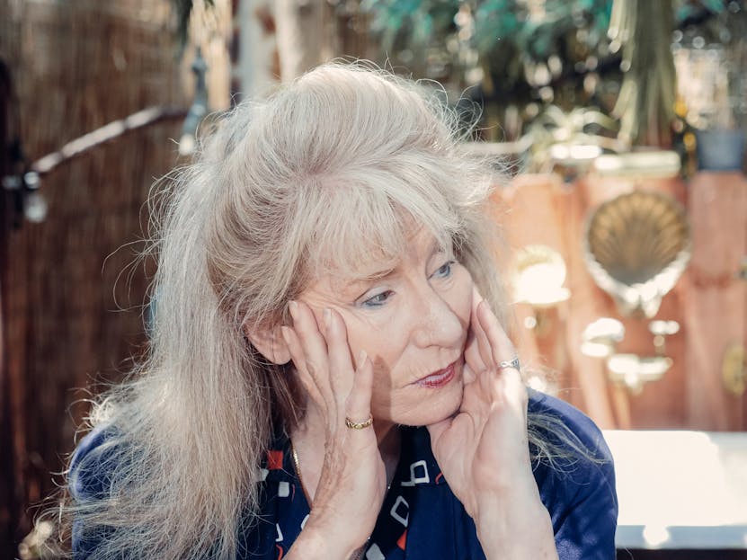 Jan Ashley Thoughtful senior woman sitting outdoors, hands on face. A reflective moment captured in sunlight.