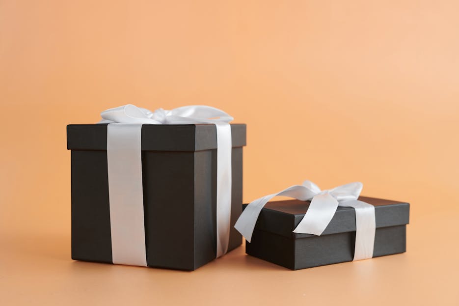 WhatUTalkingBoutWillis Gifts Two black gift boxes with white ribbons on a beige background, perfect for celebrations.